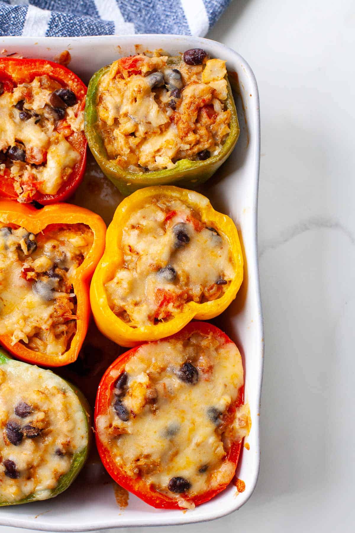 six multicolored bell peppers stuffed with cheese, rice, beans, seafood in baking dish