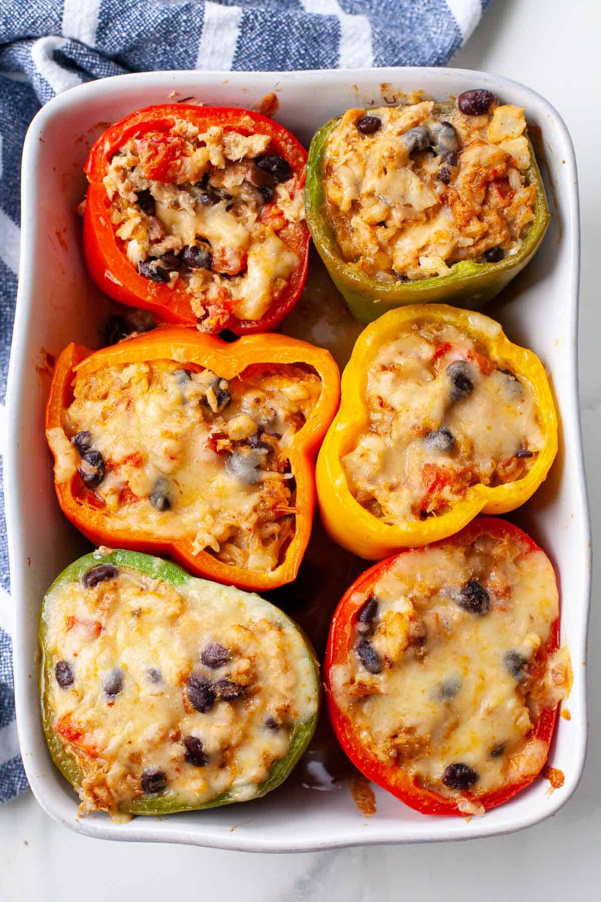 green, red, orange and yellow stuffed bell peppers in white baking dish with blue kitchen towel