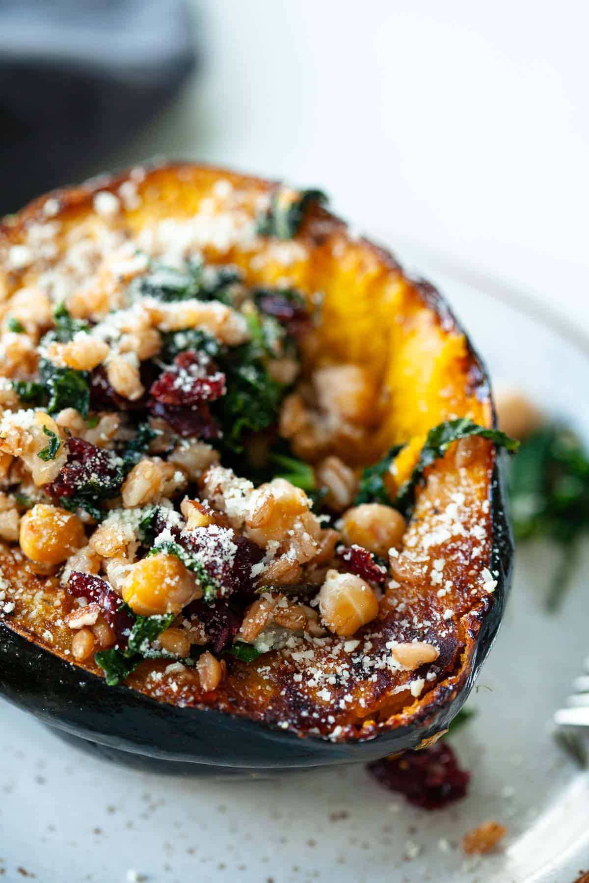 roasted acorn squash stuffed with chickpeas, kale, cranberries, farro, parmesan cheese on grey speckled plate
