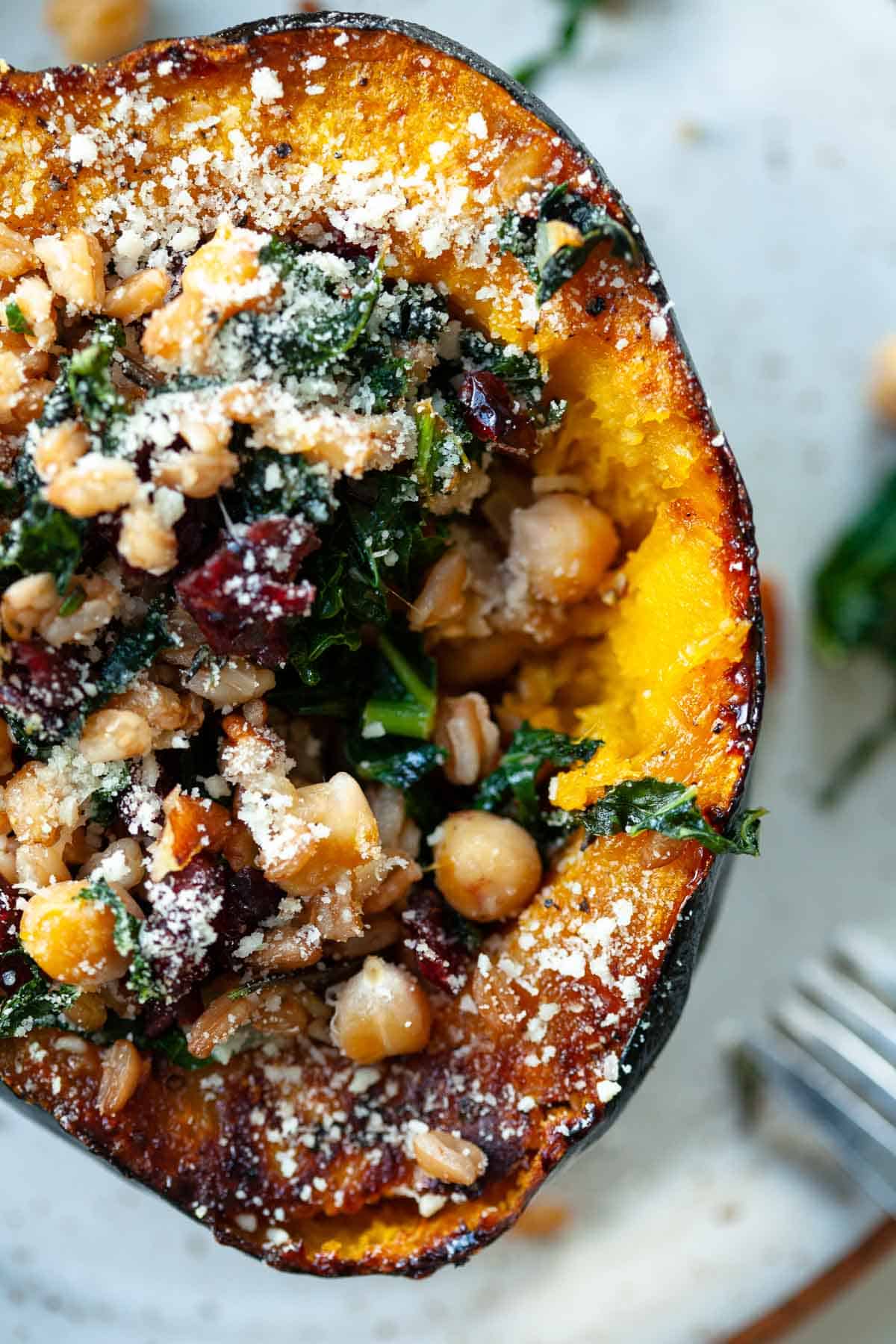 acorn squash stuffed with kale, chickpeas, farro, cranberries, pecans and parmesan cheese on grey plate