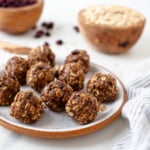 Almond Butter Protein Bites are shown on a white and orange plate with rolled oats and dried cranberries in the background