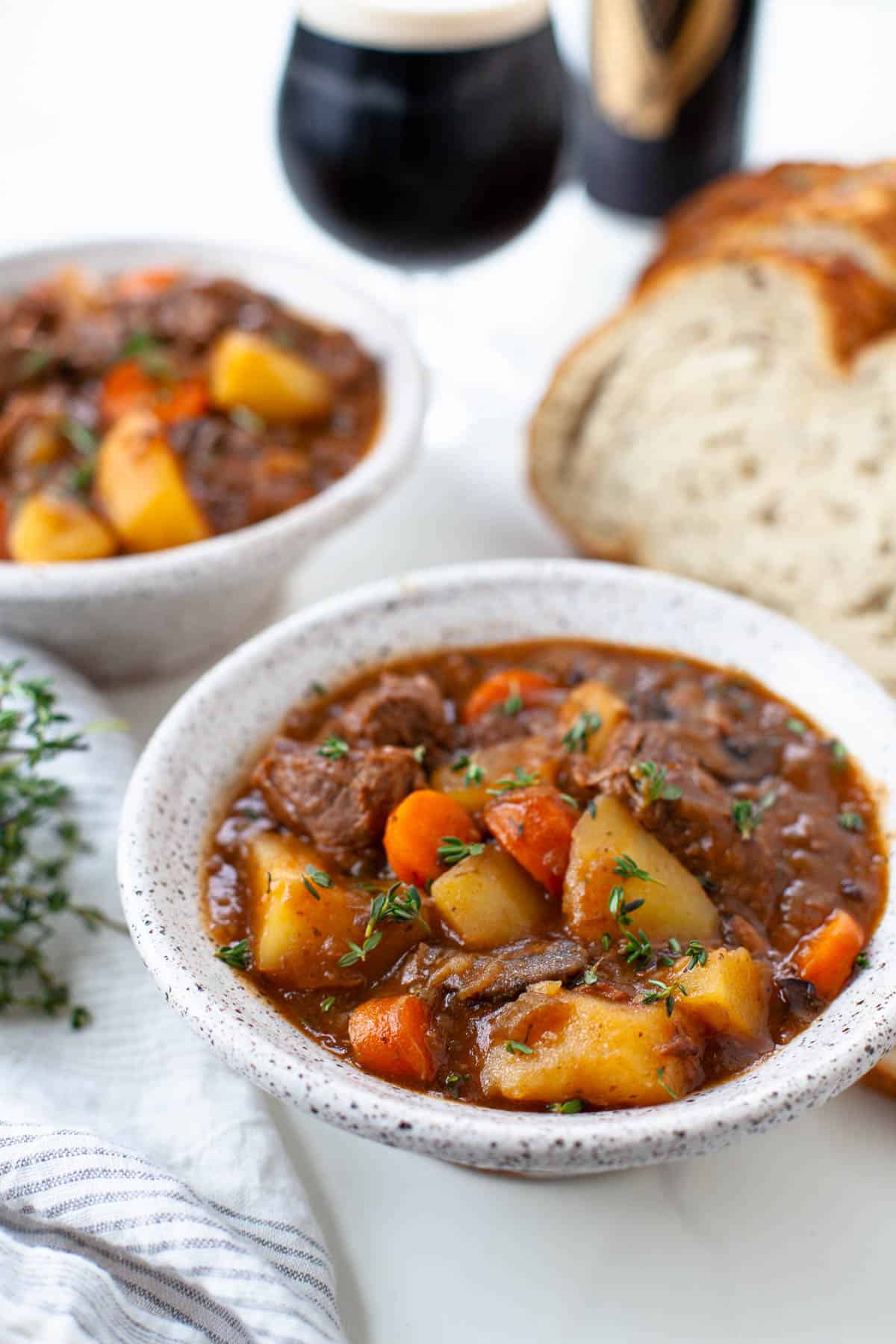 beef stew in a white speckled bowl, slices of bread, glass and can of guinness