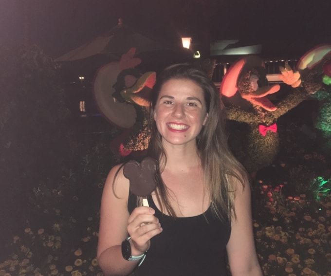 woman with red lipstick on wearing a black tank top holding a mickey mouse ice cream bar
