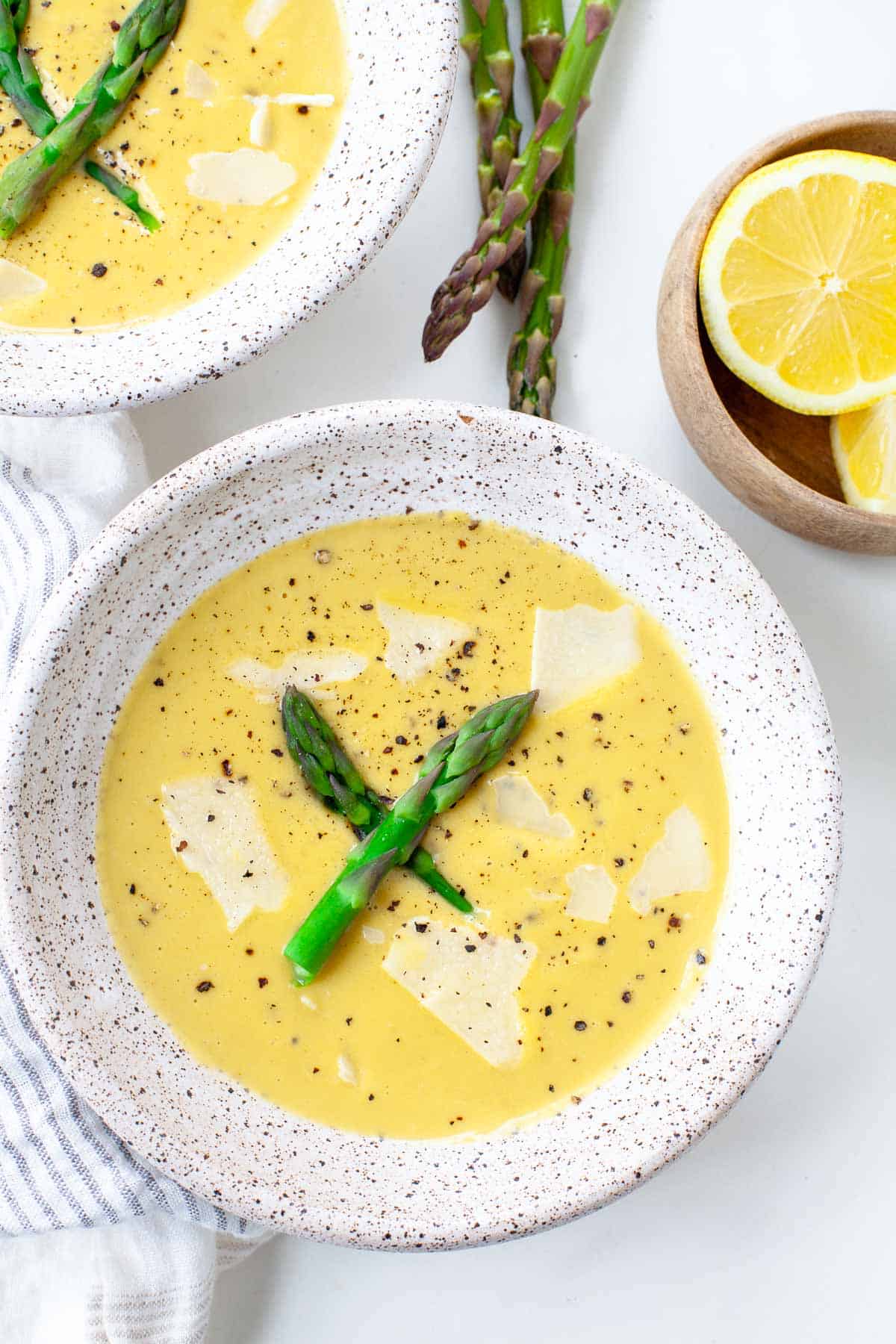 two bowls cream of asparagus soup with pepper, asparagus pieces, and lemon slices