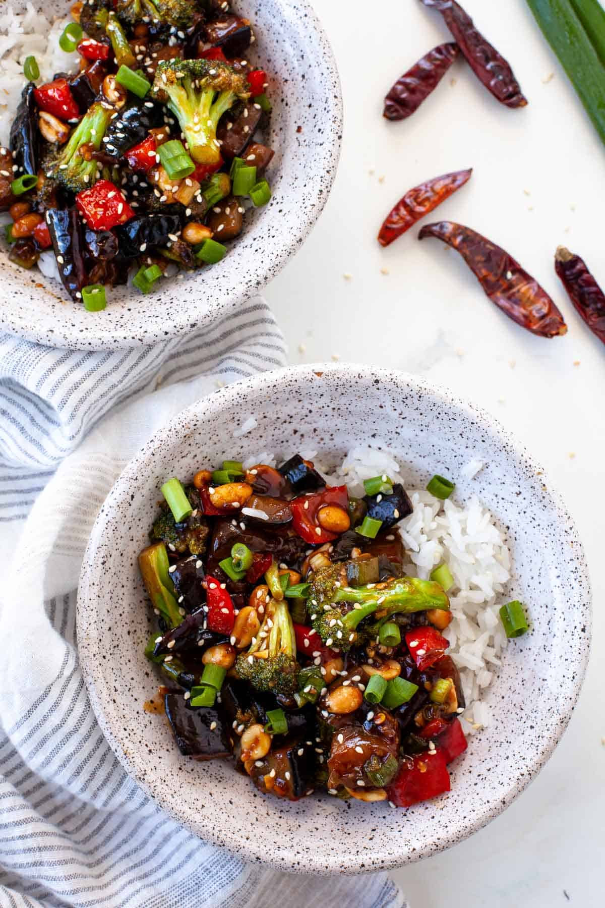 kung pao vegetables with rice in grey speckled bowls, dried chilis and striped dish towel