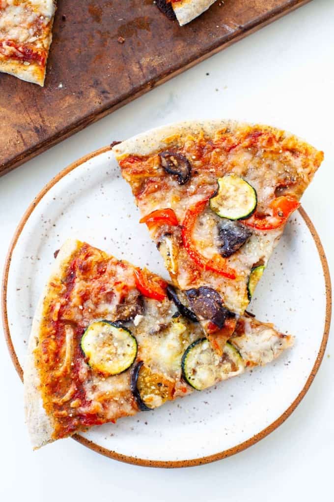 two roasted vegetable pizza slices on white speckled plate 