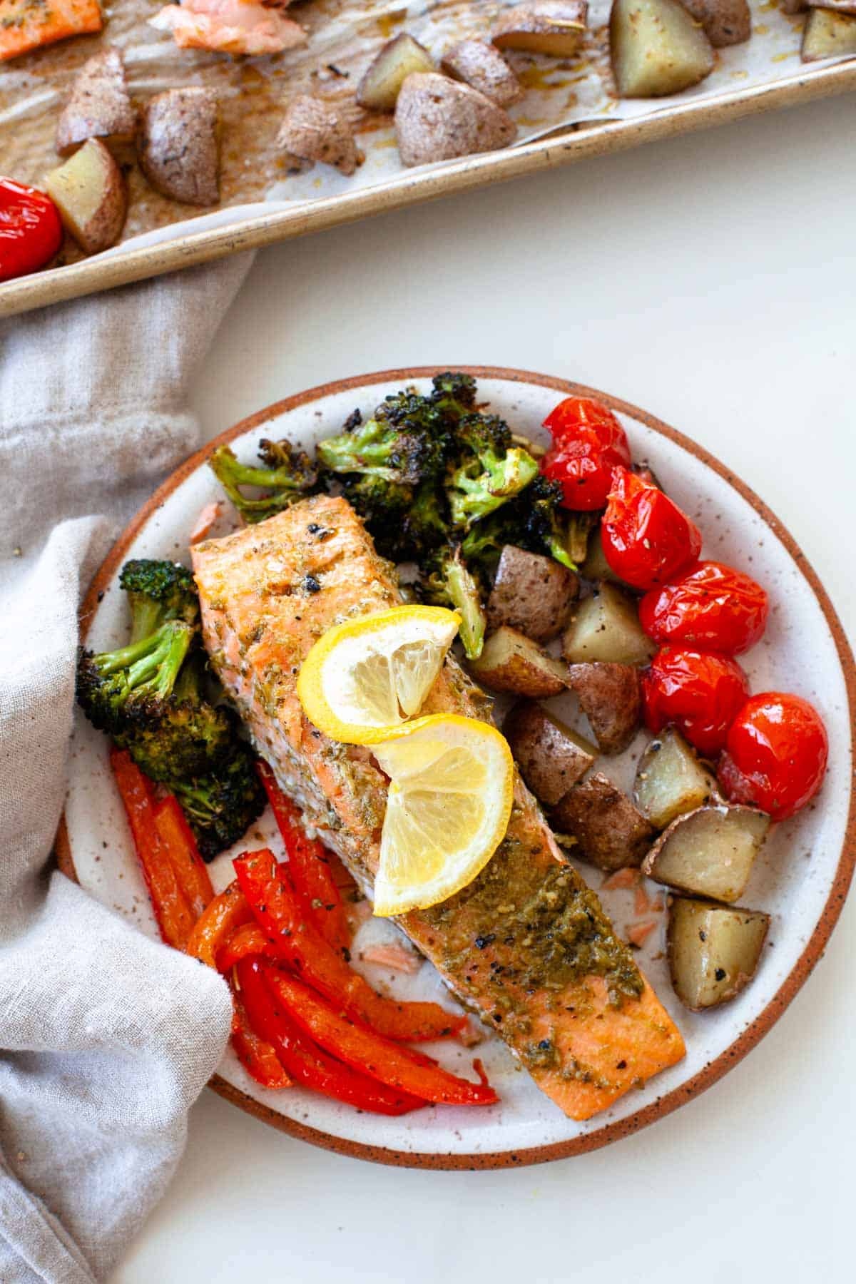 sheet pan salmon with tomatoes, potatoes, broccoli, bell pepper and lemon on speckled plate