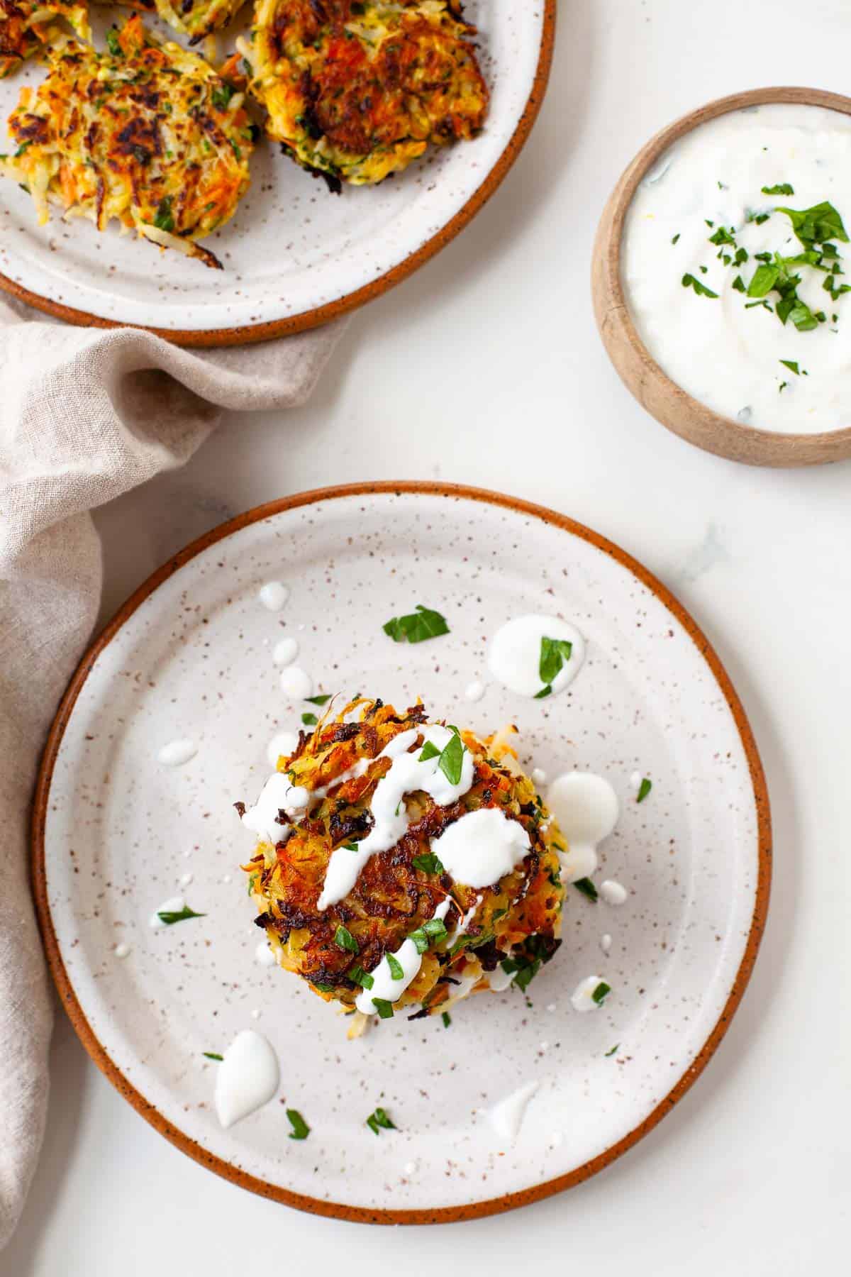two plates of kohlrabi fritters with a side of parsley herb yogurt sauce on top