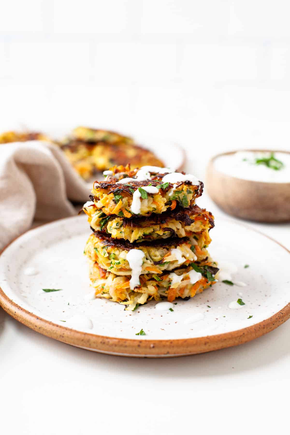 stack of four kohlrabi fritters on a speckled plate with herb yogurt sauce drizzled on top