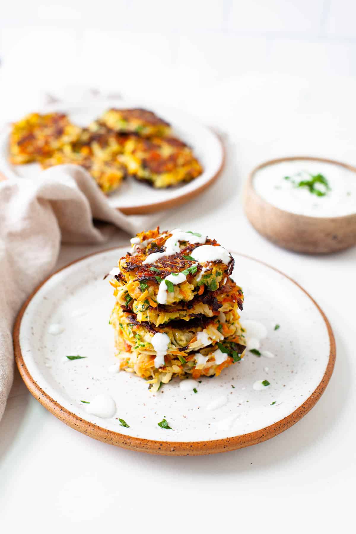 stack of four kohlrabi fritters on a speckled plate with herb yogurt sauce and parsley on top