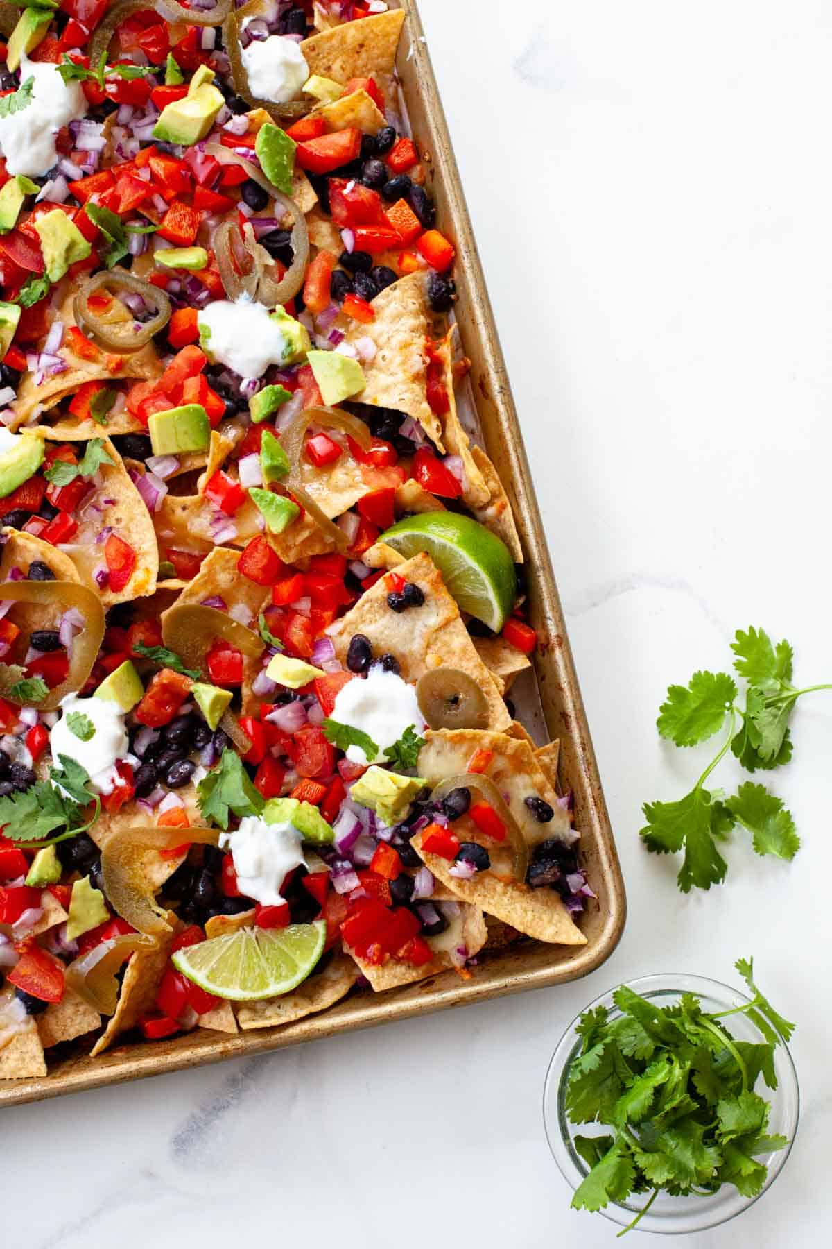 vegetarian nachos on a sheet pan over white marbled background and a side of cilantro 