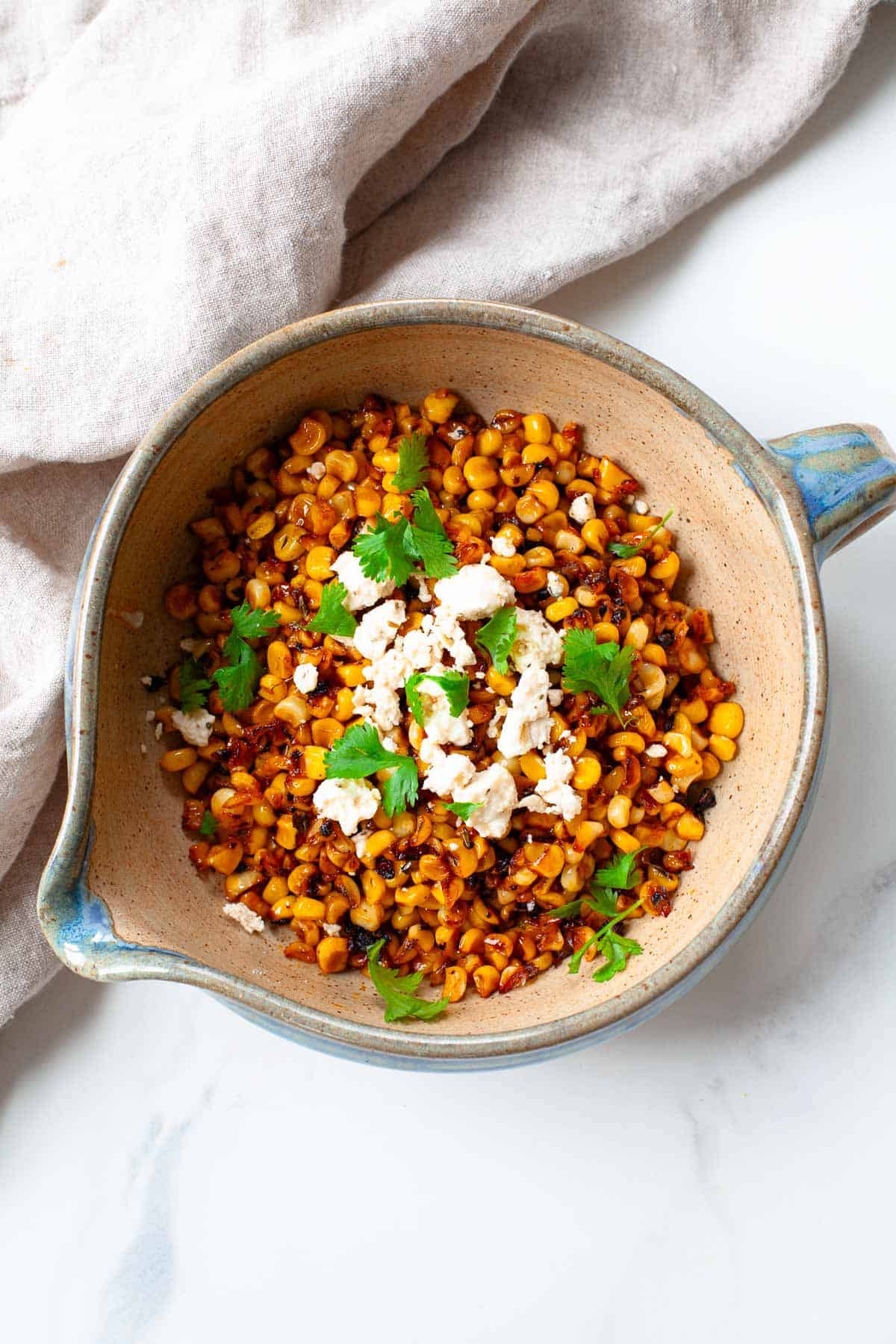 blackened corn in a bowl with a mango topped with fresh cilantro and crumbled feta next to a kitchen towel