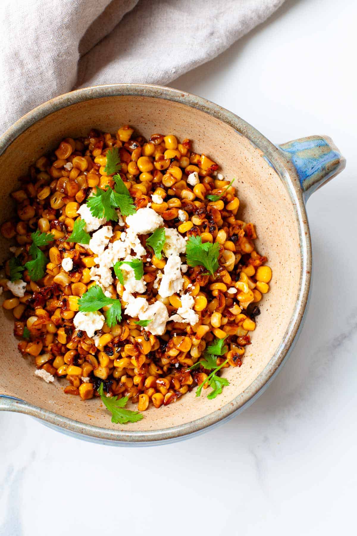 blackened corn in a blue and tan bowl garnished with cilantro and crumbled feta