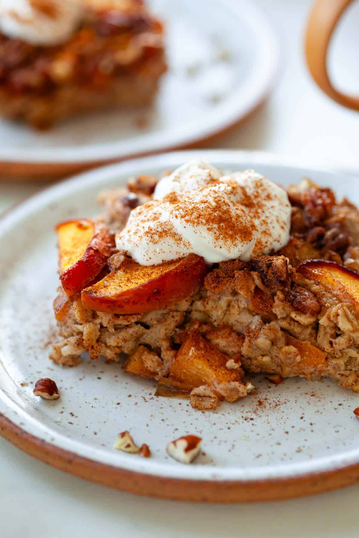 peach baked oatmeal with dollop of yogurt and sprinkled cinnamon on white speckled plate