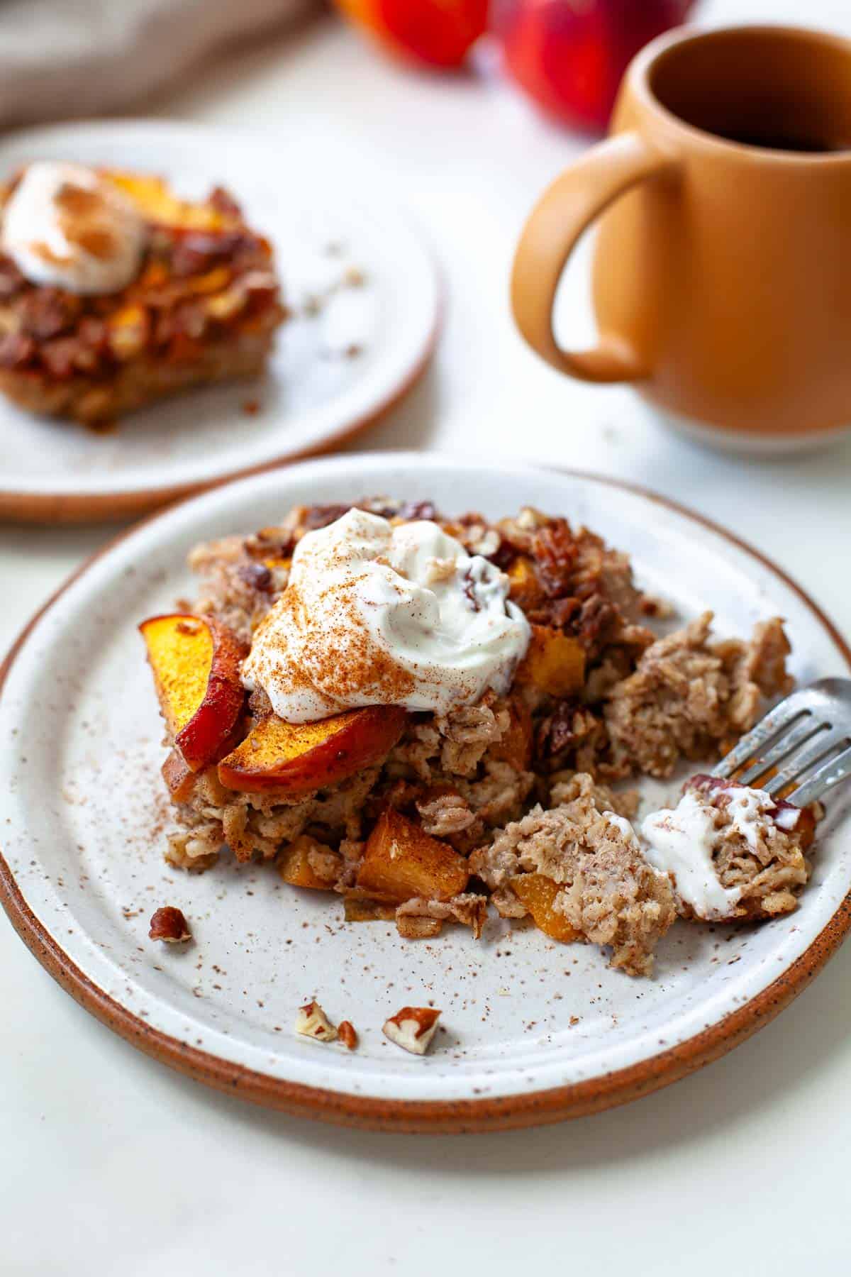 two peach baked oatmeal on white speckled plates topped with yogurt and cinnamon
