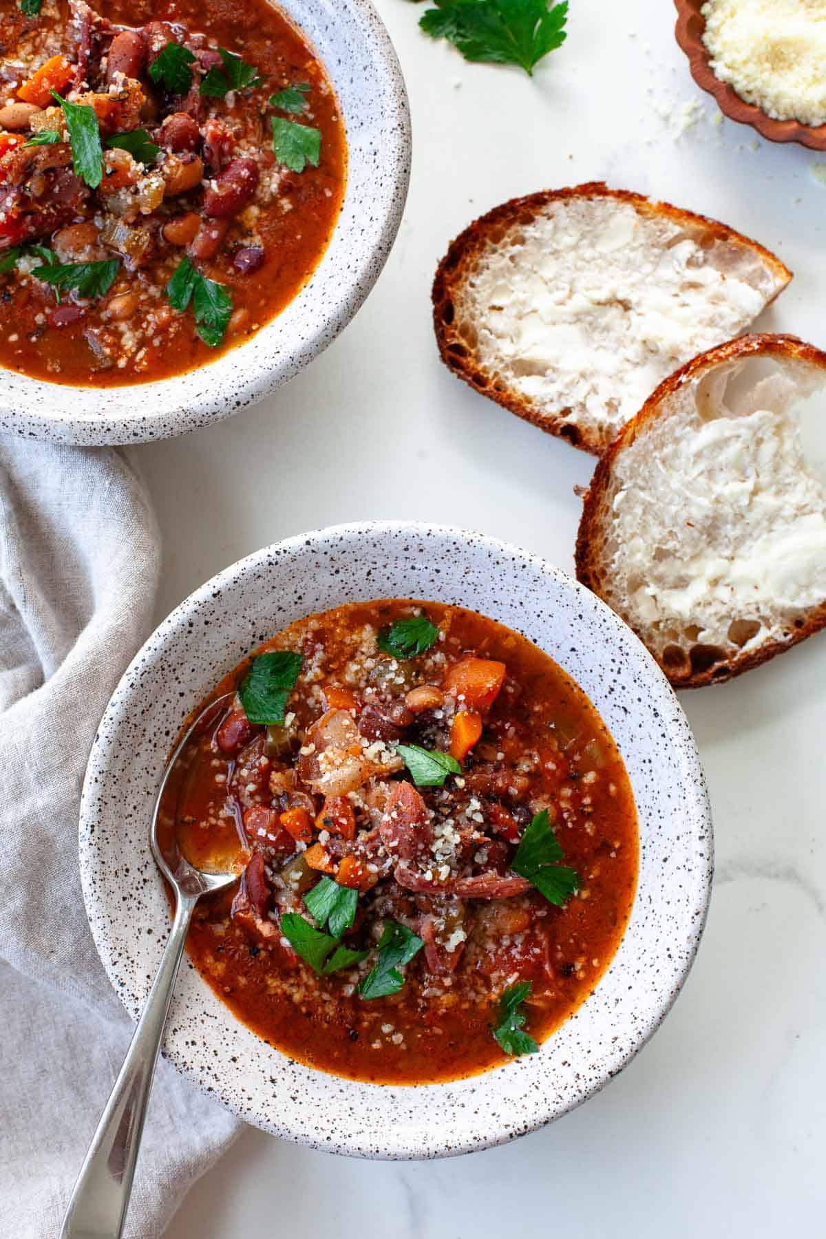 two bowls of instant 15 bean soup seasoned with black pepper, parmesan cheese and parsley alongside two pieces of fresh artisan bread