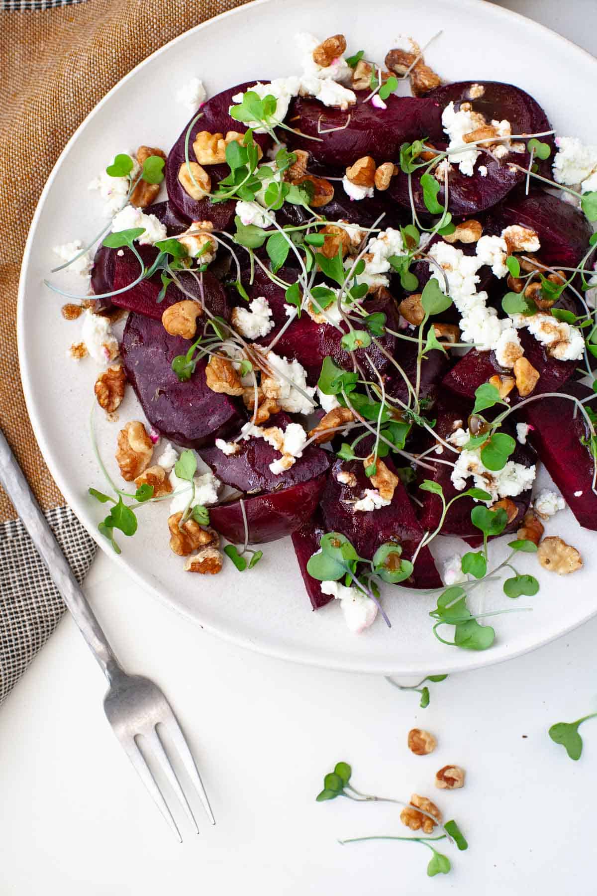 Beet salad with feta cheese on a white plate next to a kitchen towel and a small silver fork