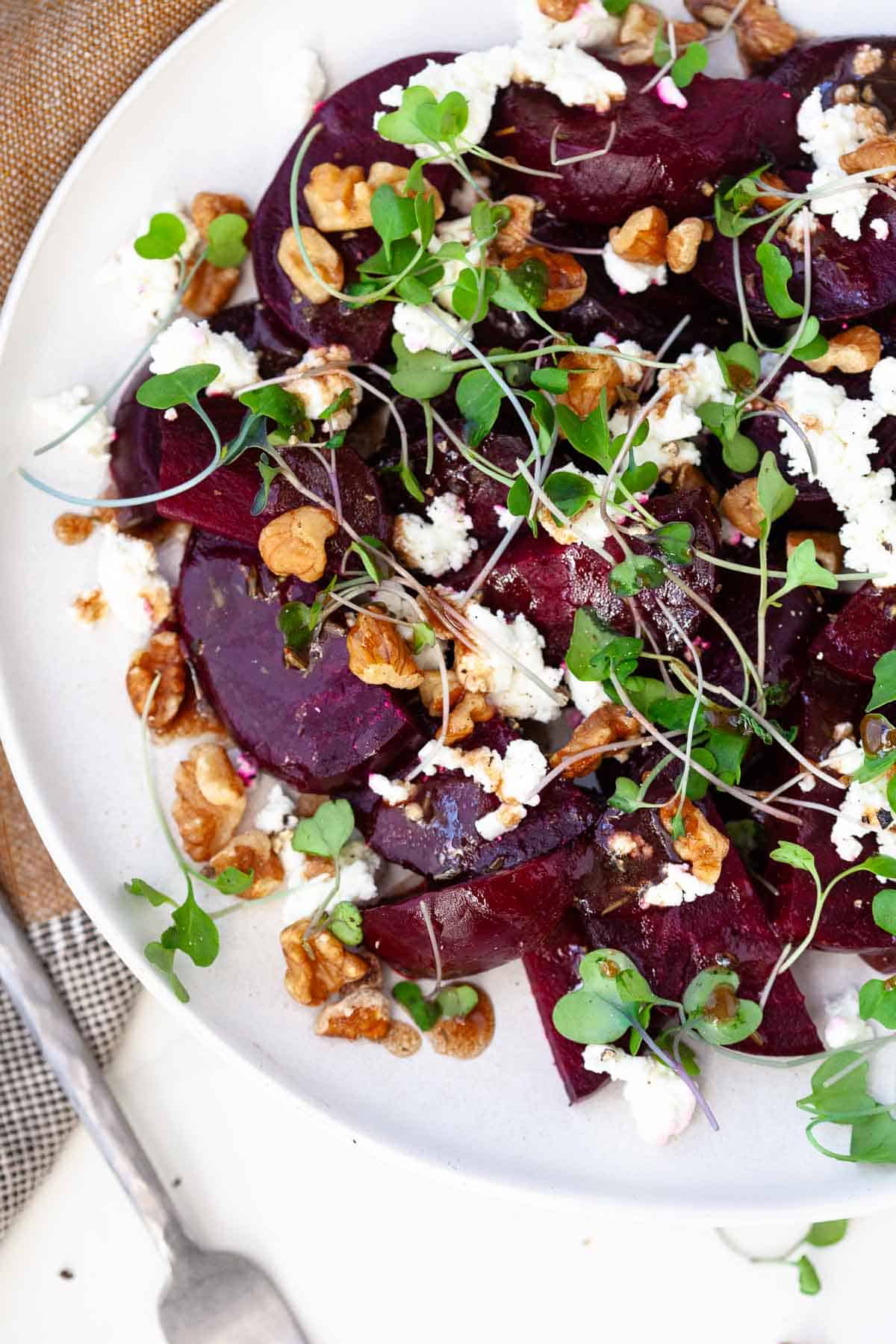 beetroot salad with feta on white plate with roasted beets, crumbled feta cheese, toasted walnuts, and microgreens