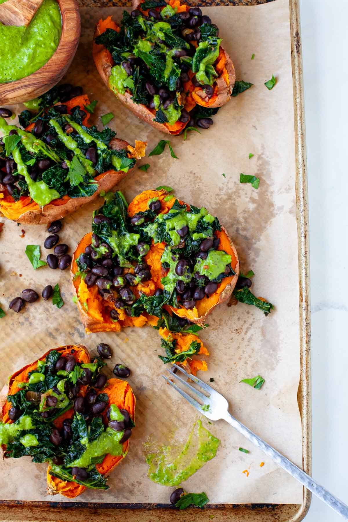 Vegan loaded sweet potatoes with green goddess dressing on a parchment paper-lined baking sheet.