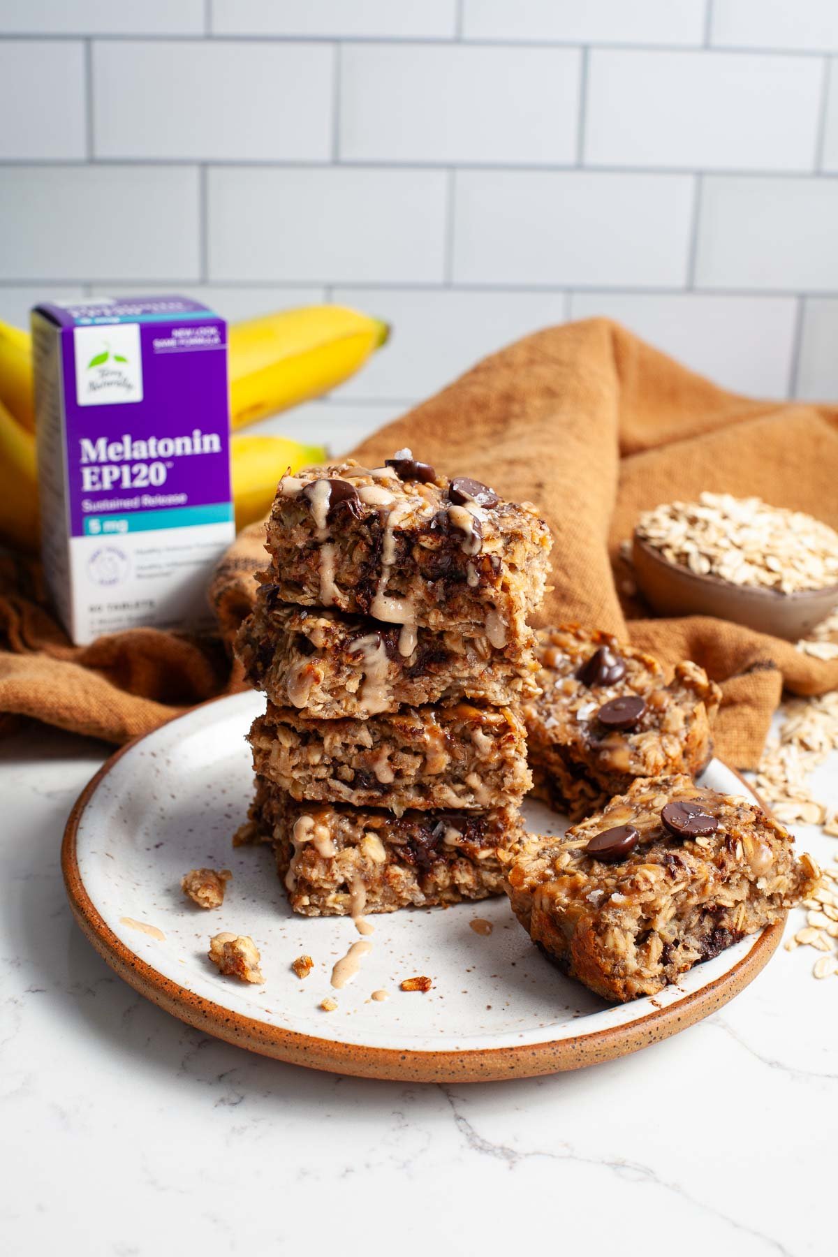 peanut butter banana oat bars with chocolate chips stacked on a plate with supplement box in background