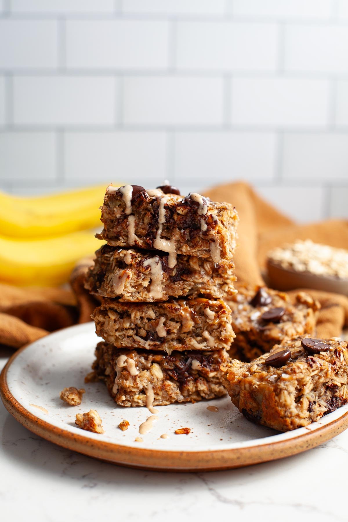 four peanut butter banana oat squares stacked on top of each other with two more on plate