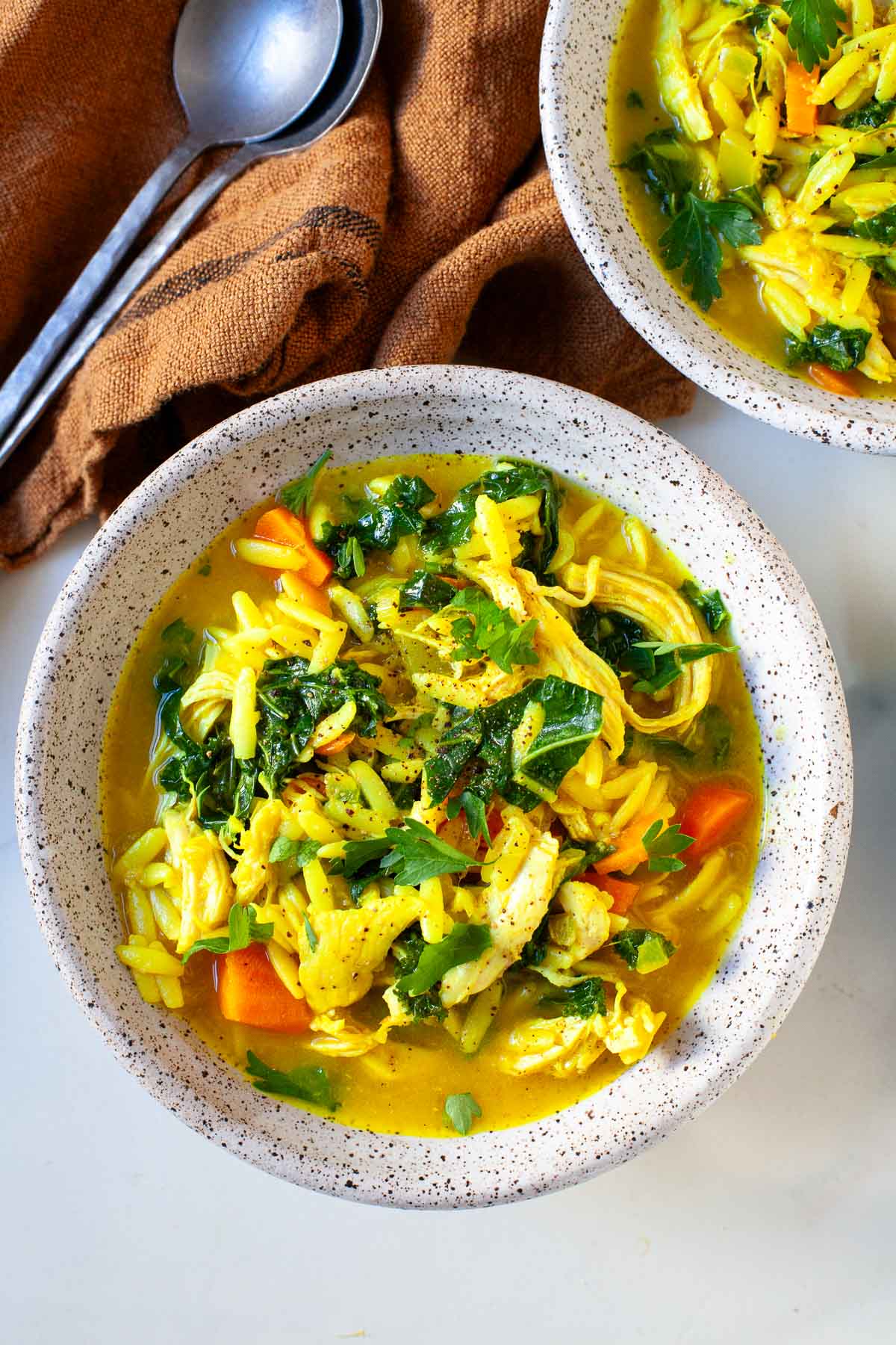 speckled grey bowl with chicken orzo soup with turmeric, kale, carrots and parsley on top