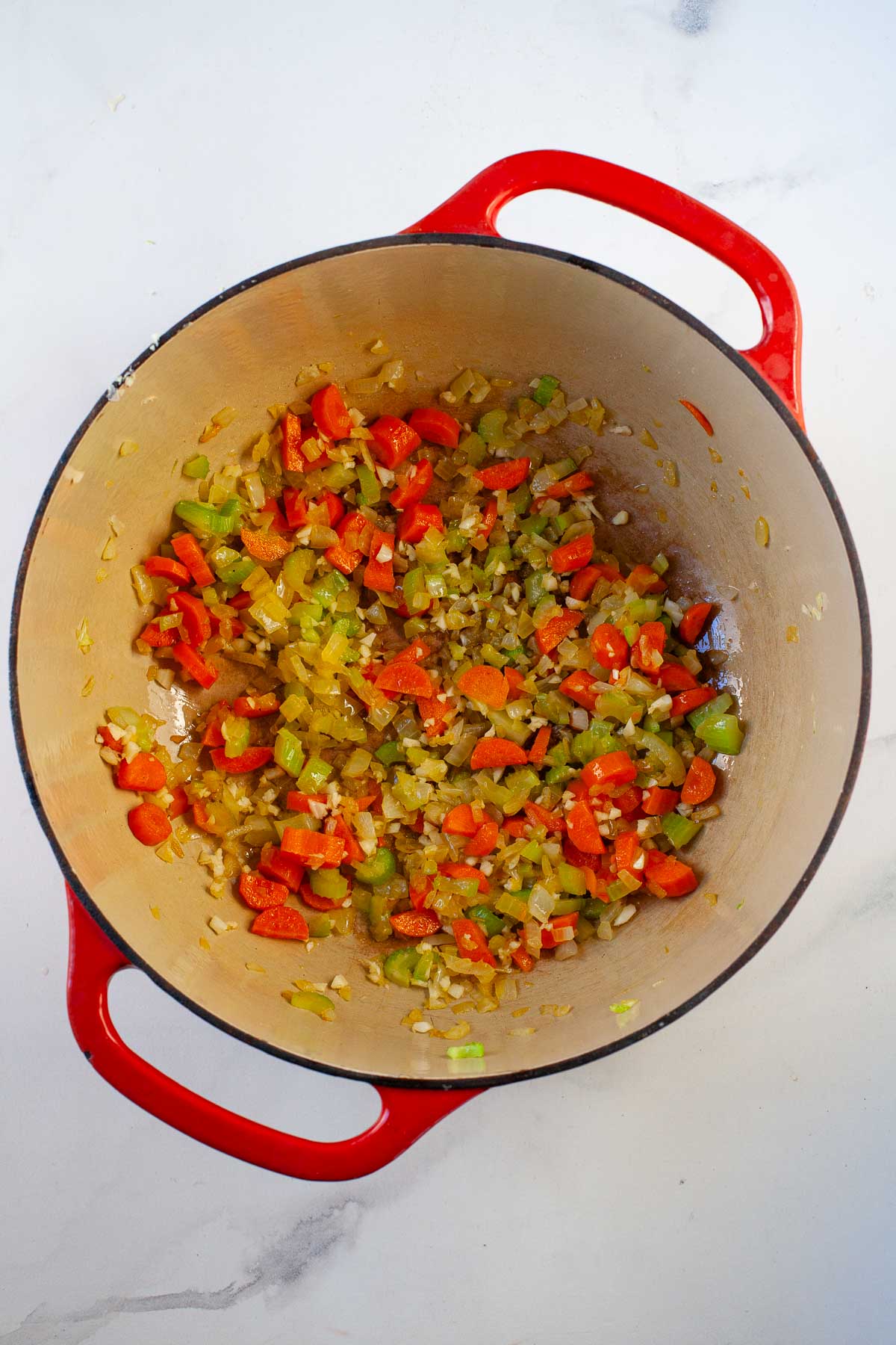 carrot, onion, celery and garlic cooked in a red dutch oven on marble surface