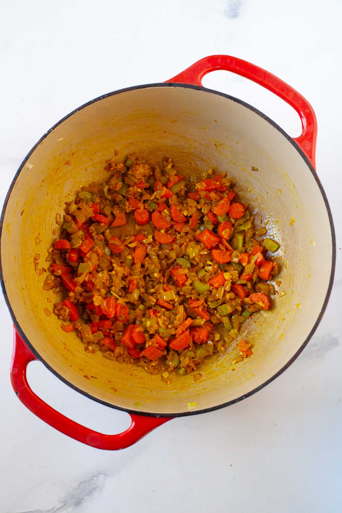 carrot, celery, onion, turmeric and ginger cooked in a red dutch oven on marble surface