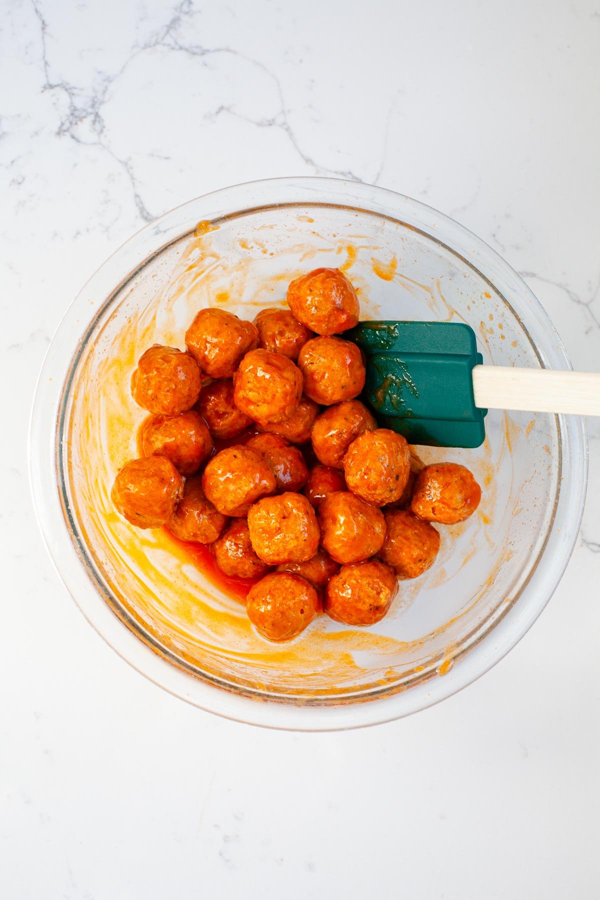 buffalo chicken meatballs tossed with Frank's hot sauce in glass bowl