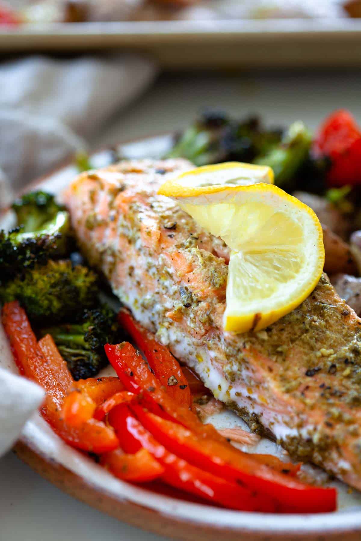 baked salmon with pesto and lemon on top next to bell peppers and broccoli