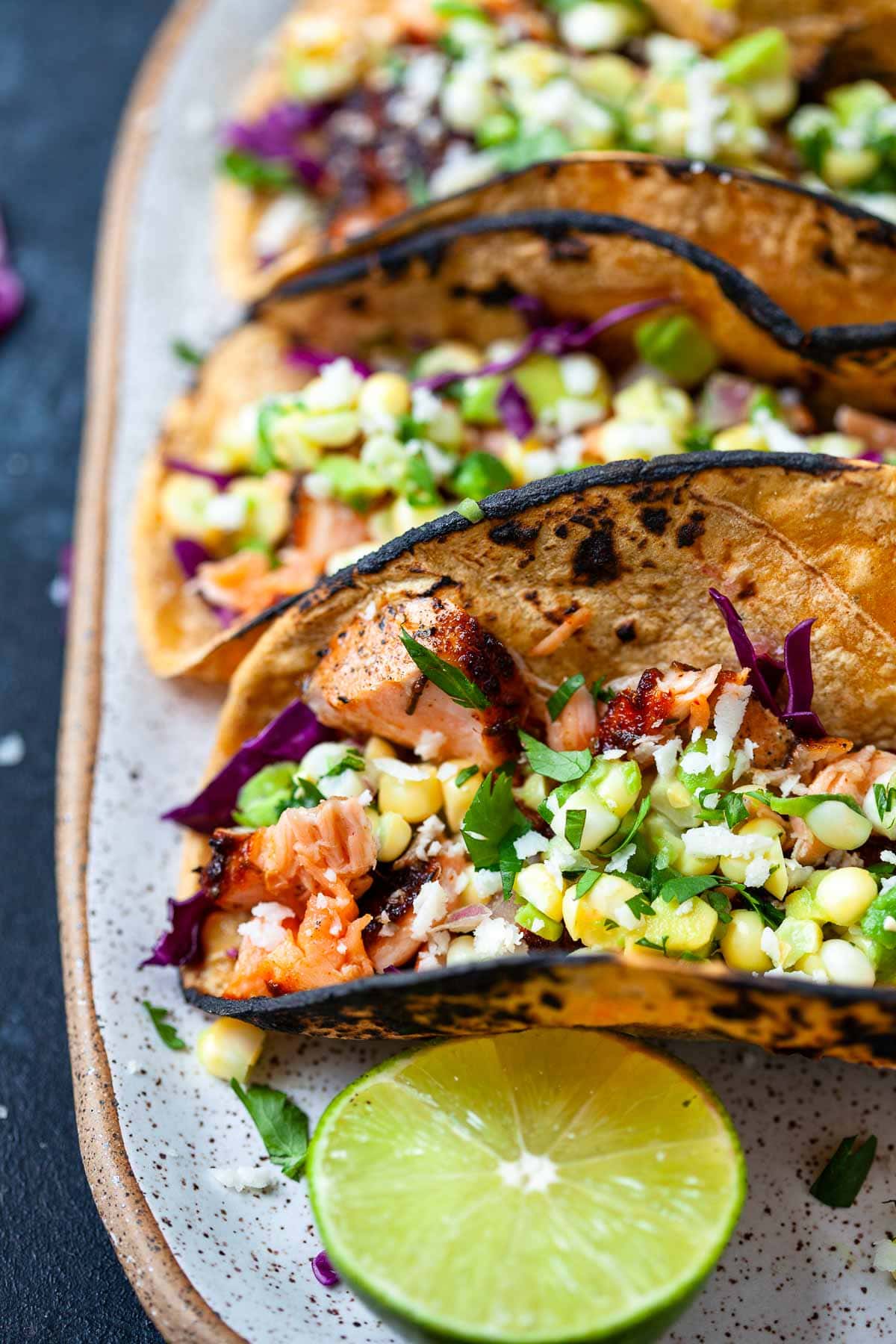 three blackened salmon tacos covered in corn avocado salsa next to lime wedge