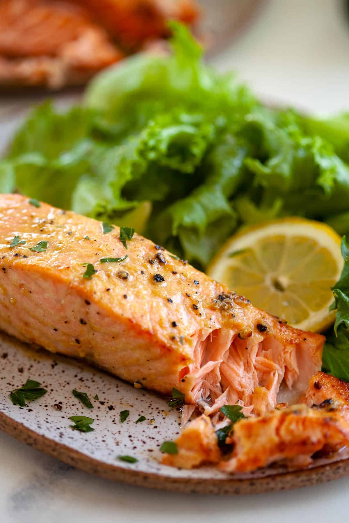 flaky air fryer salmon next to salad greens and lemon slice