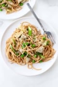 spring vegetable pasta with asparagus, peas, artichokes on white plate with fork white background